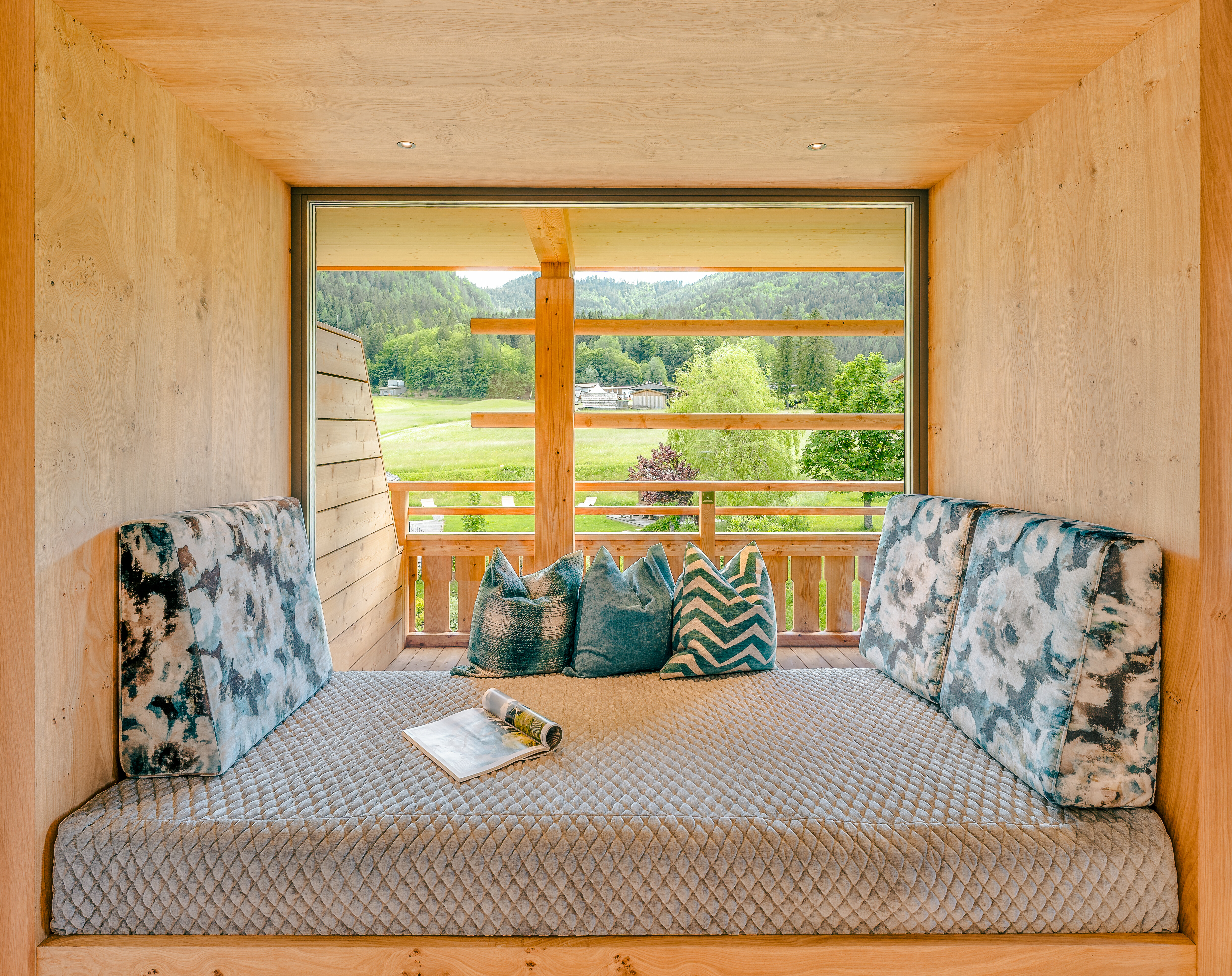 Cozy seating area with cushions and a magazine, offering a view of nature through a large window.