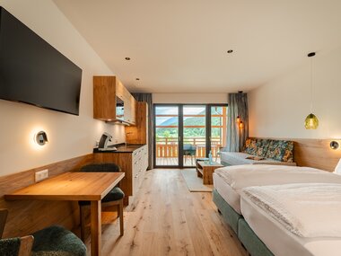 Modernes Hotelzimmer mit Doppelbett, Küchenecke und Balkon mit Blick auf die Natur.