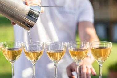 Ein Barkeeper gießt einen Drink aus einem Shaker in fünf Cocktailschalen, die auf einer Bar stehen.