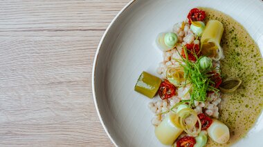 Ein kunstvoll angerichtetes Gericht mit Getreide, Lauch, getrockneten Tomaten und grüner Sauce.