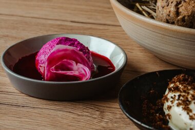 A serving of bright pink dessert on a white plate, accompanied by a red sauce, with two other bowls of food in the background.