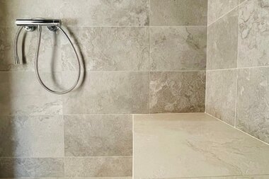 Modern shower with gray tiles and a built-in shelf for toiletries.