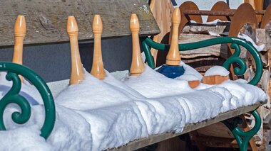 An outdoor bench covered in snow, next to wooden figures resembling sculptures.