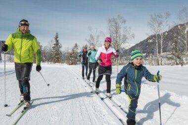 Eine Gruppe von Menschen, die auf einer verschneiten Strecke Ski fahren, umgeben von winterlichen Bäumen und Bergen.