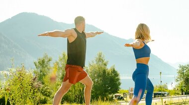 A man and a woman practicing yoga outdoors with a mountain landscape in the background.