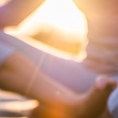 A person meditating in a yoga pose, sitting cross-legged on a mat in a field during sunset.