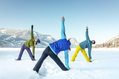 Three people stretching in the snow against a mountain landscape.